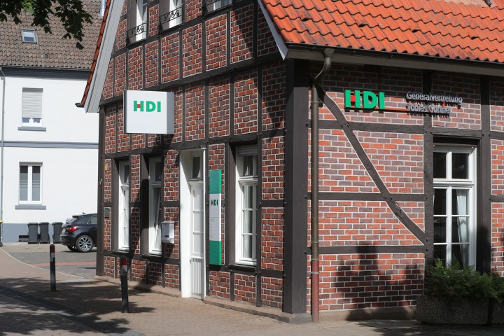 Blick von außen auf das Agenturgebäude. Dieses ist ein Backsteingebäude mit HDI Werbung an der Fassade.