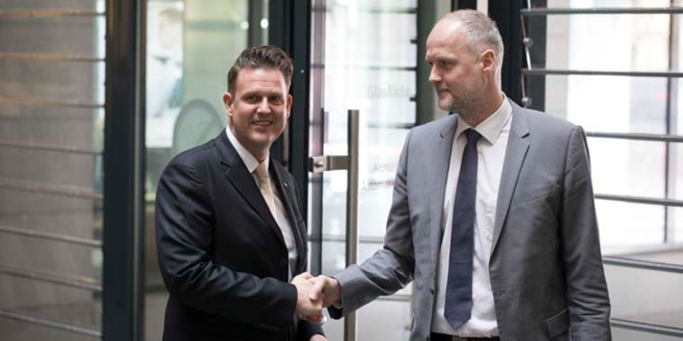 Ulf Hauck links und ein Mitarebiter rechts stehen auf einem Flur und geben sich die Hand