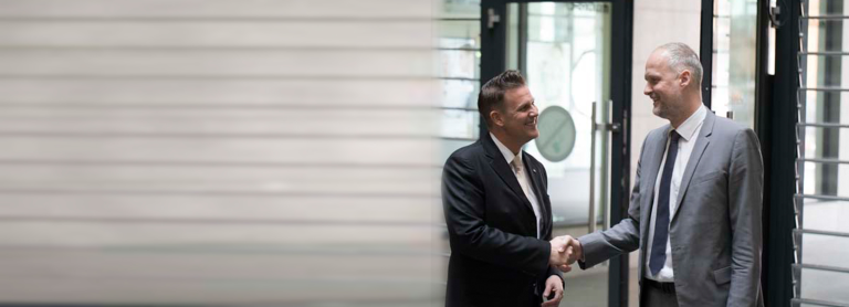 Ulf Hauck links und ein Mitarebiter rechts stehen auf einem Flur und geben sich die Hand