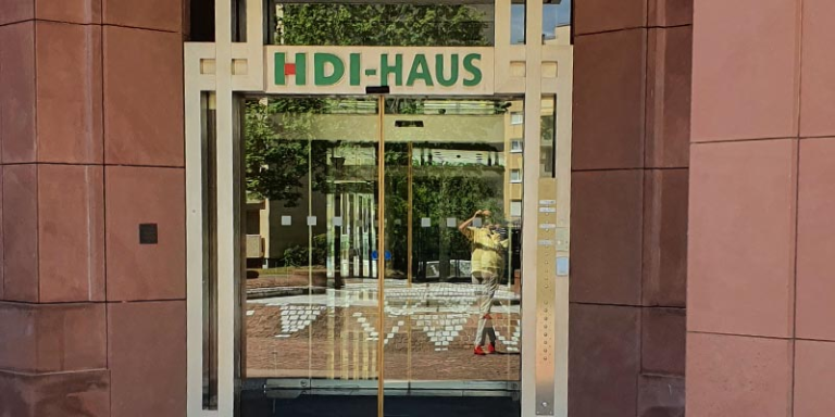 Der Eingang der agentur befindet sich in einem rötlichen Gebäude und hat eine Glastür. Über der Tür steht in grün HDI-Haus
