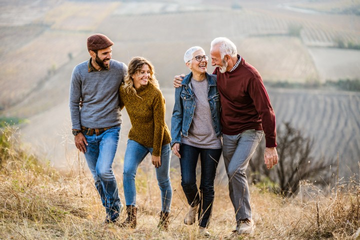 Zwie Paare unterschiedlicher Generationen laufen umarmt durch die natur bei Abendsonne