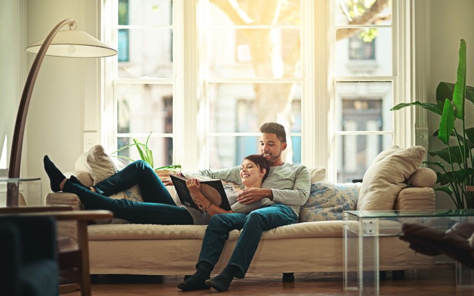 Paar, das zusammen auf der Couch liegt und in einem Buch liest.