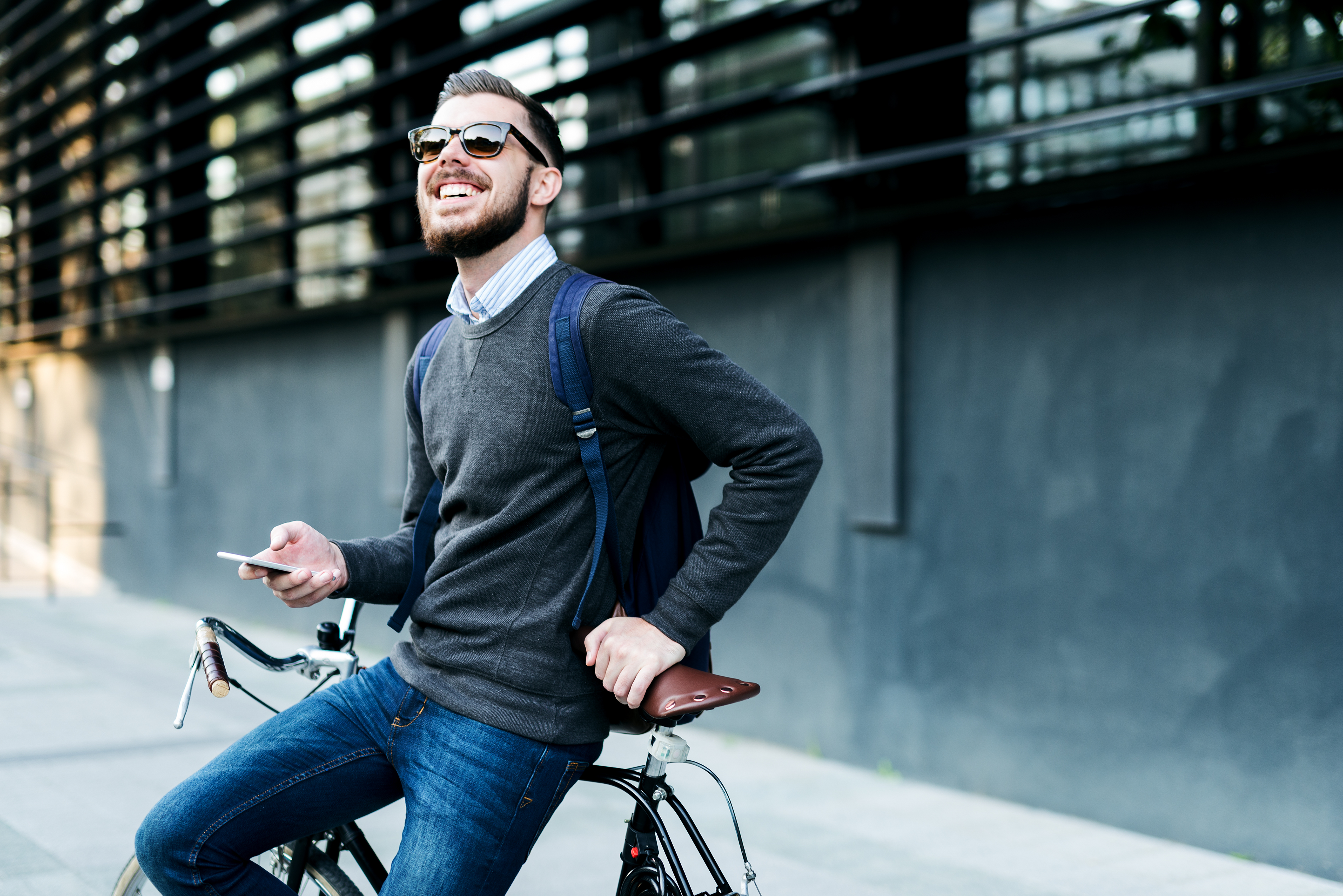 Man der sich lachend an sein Fahrrad lehnt und sein Handy in der Hand hält