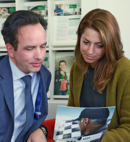 Man sieht Stephan Hecker und eine Frau die sich zusammen eine Art BRoschüre von HDI anschauen. Im Hintergrund sieht man eine Auslage, auf der noch andere Prospekte von HDI zu finden sind.