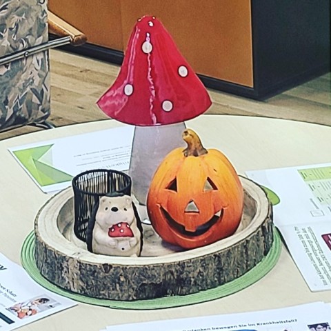 Auf einem Tische steht ein Holzteller und auf dem steht ein Pliz, ein Kürbis und ein Igel