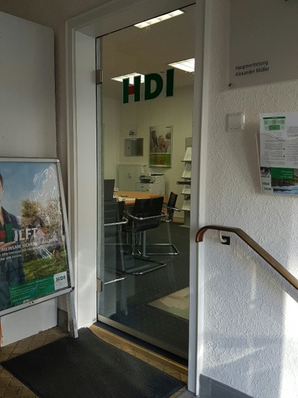 Durch eine Glastür kann man in die Agentur hereinschauen und sieht einen Tisch mit mehreren Stühlen sowie Werbung von HDI in Form von Plakaten und Flyrn in einem Aufsteller.