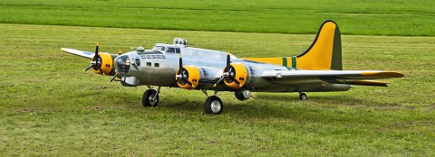 Grauer Modellflieger mit gelben Details und Propellern, der auf einem grünen Feld steht.
