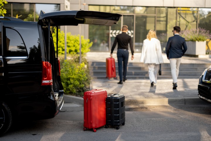 Auto vor einem Hotel. Am Kofferraum sthen zwei Koffer.