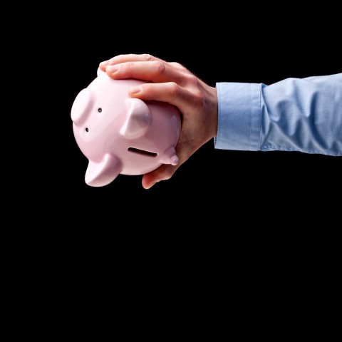 Hand hält leeres Sparschwein in der Hand mit der Öffnung nach unten.
