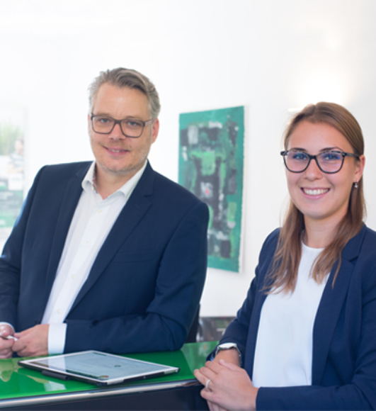 Jan Georg Weyers und Laura Marie Heidschuster stehen gemeinsam am Empfangstresen, zwischen ihnen liegt ein Tablet
