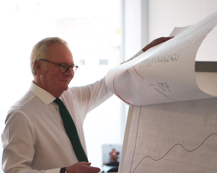 Michael Jansweid der gerade die nächste Seite auf einem Flipchart umblättert. Auf dem Flipchart sind Zeichnungen von Diagrammen und Grafiken.