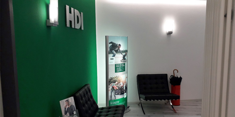 Agentur von innen, links grüne Wand mit HDI Logo und ein schwarzer Stuhl, geradezu HDI Ständer und danben schwarzer Stuhl, rechts Heizung
