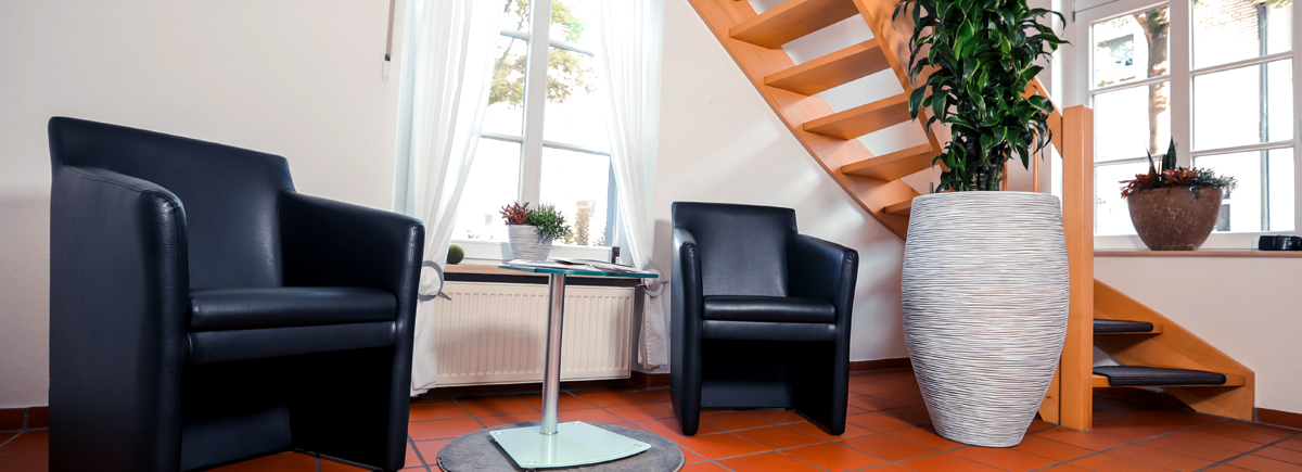 zwei schwarze Ledersessel stehen vor einem Fenster, daneben führt eine Holztreppe in das Obergeschoss des Hauses