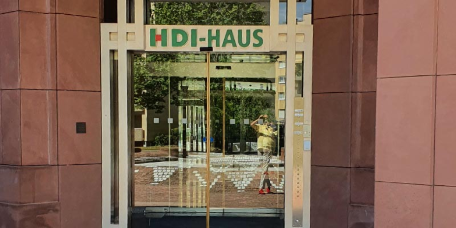 Der Eingang der agentur befindet sich in einem rötlichen Gebäude und hat eine Glastür. Über der Tür steht in grün HDI-Haus