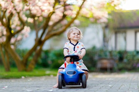 Kind sitzt auf einem blauen Bobbycar und fährt damit.