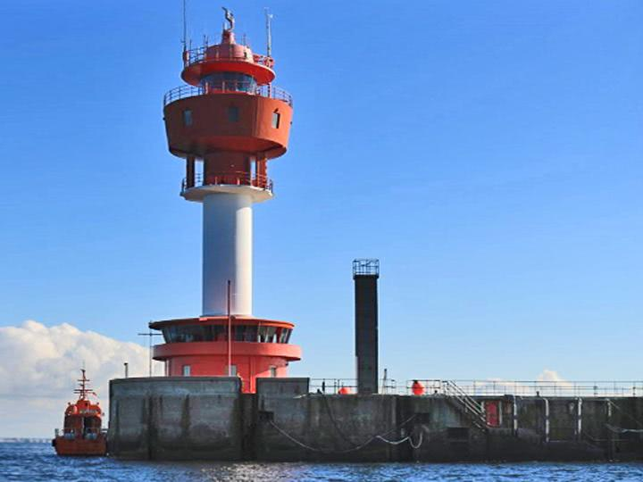 In der Mitte ist ein Leuchttum mit einem grauen Steg, bleuem wasser und blauem Himmel