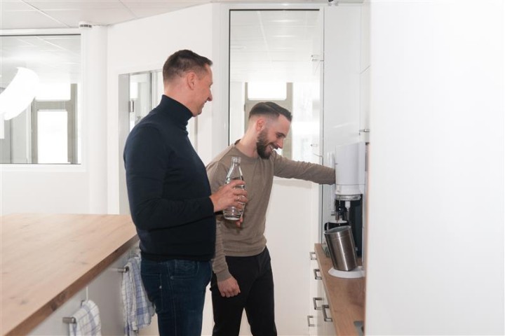 Scheffler und ein Mitarbeiter stehen in der Küche und lachen dabei.