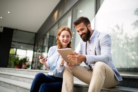 Ein Mann und eine Frau sitzen gemeinsam und schauen auf ein Tablet. Die Szene zeigt eine entspannte Beratungssituation im Alltag.