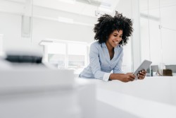 Lächelnde Frau mit Afro-Frisur nutzt ein Tablet in einem modernen Büro