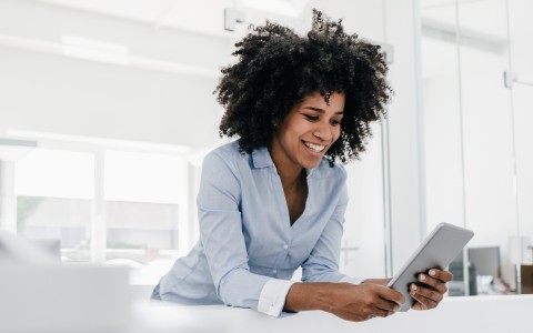 Lächelnde Frau mit Afro-Frisur nutzt ein Tablet in einem modernen Büro