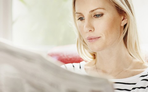 HDI Pressemeldungen: Blonde Frau sitzt auf einem roten Sofa und schaut etwas auf dem Laptop