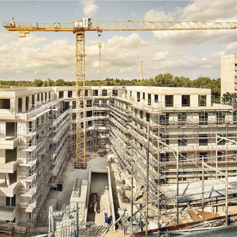 Blick auf eine Großbaustelle eines weitläufigen Brürokomplexes in U-Form, in der Mitte steht ein riesiger gelber Kran
