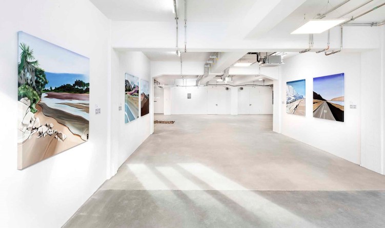 Moderne Bilder, die in einer Art weißer Tiefgarage hängen, an der Decke silberne Luftschächte