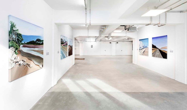 Moderne Bilder, die in einer Art weißer Tiefgarage hängen, an der Decke silberne Luftschächte