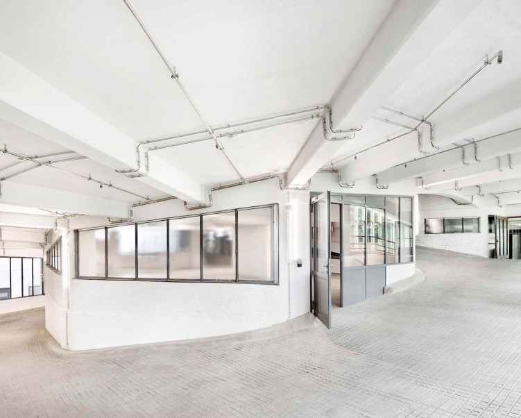 Kreisförmige Auffahrt eines Parkhauses mit weiß getünchten Wänden und Decken und silbernen Lüftungsrohren an der Decke