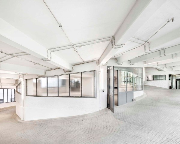 Kreisförmige Auffahrt eines Parkhauses mit weiß getünchten Wänden und Decken und silbernen Lüftungsrohren an der Decke