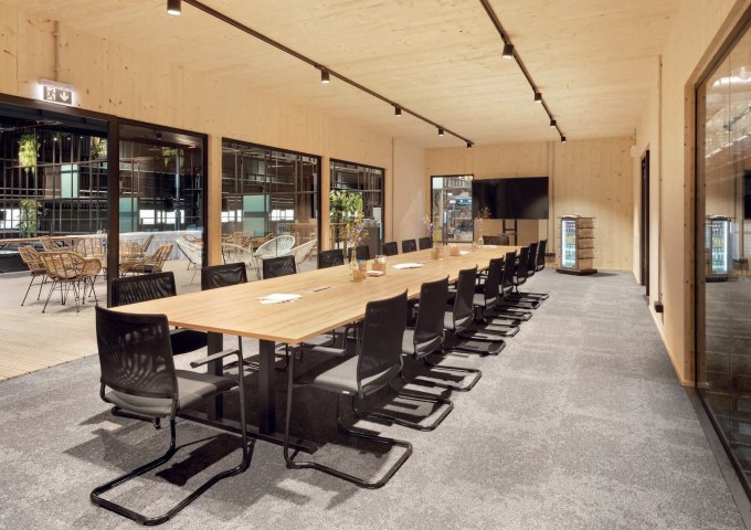 Verglaster Konferenzraum mit heller Holzvertäfelungen an Wänden und Decken, passendem Konferenztisch, schwarze Hängesessel um den Tisch und schwarzen Spots an der Decke