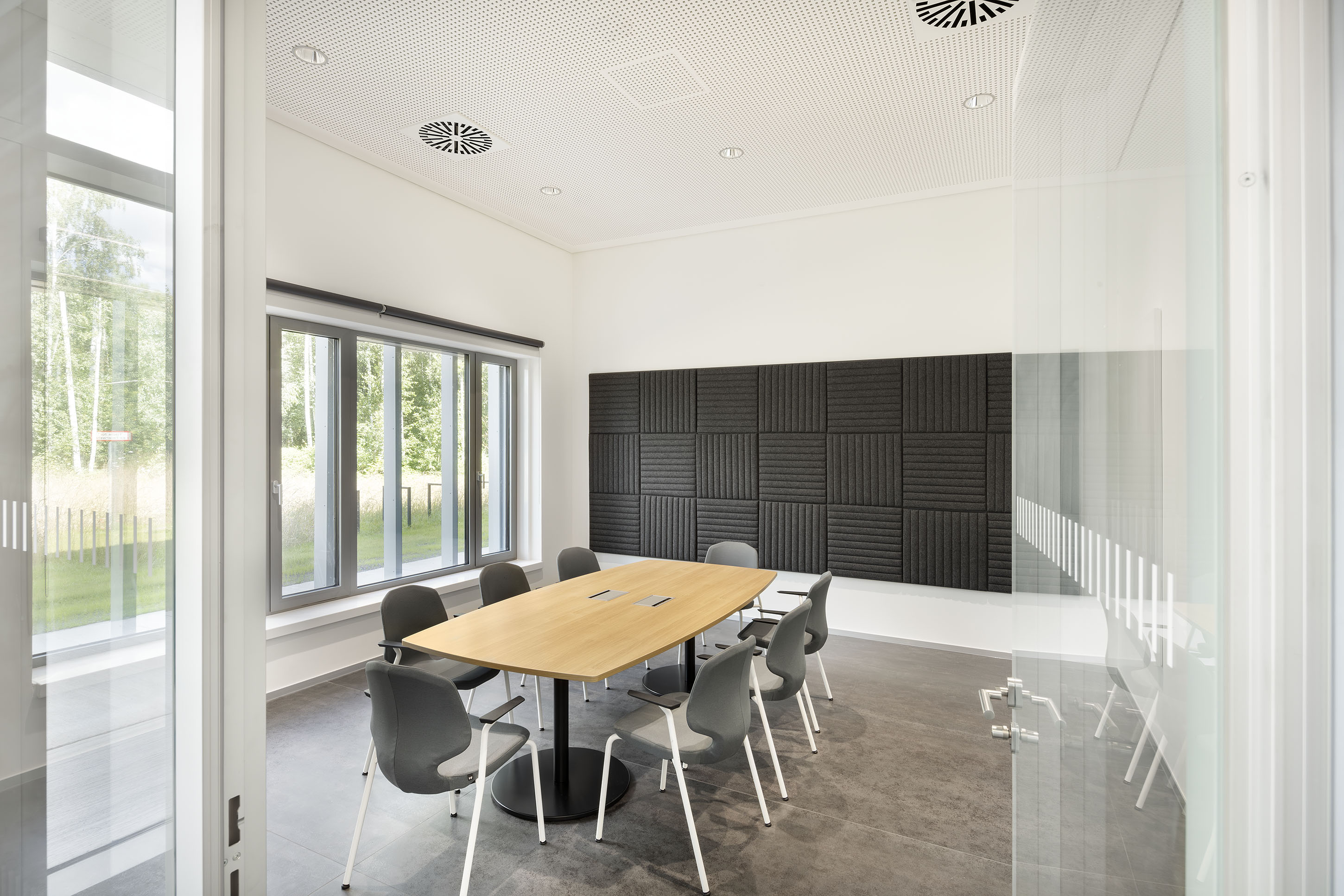 Konferenzraum mir hellem Holztisch, großer Fensterfront und anthrazitgrauen Akkustikpanelen an der Wand