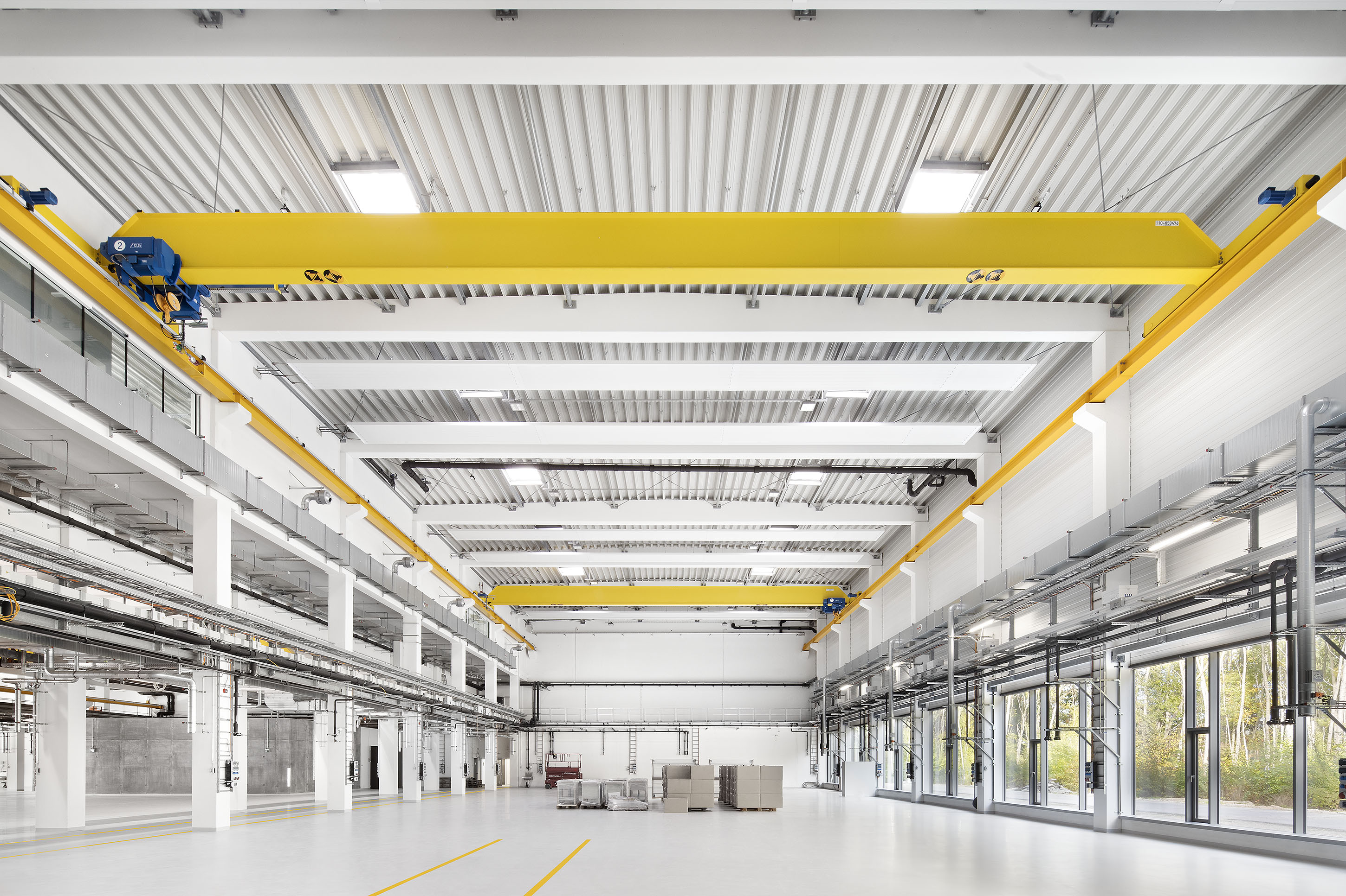 Große, weiße, leere und sehr moderne Produktionshalle mit gelben Stahlträgern und silbernen Lüftungsschächten
