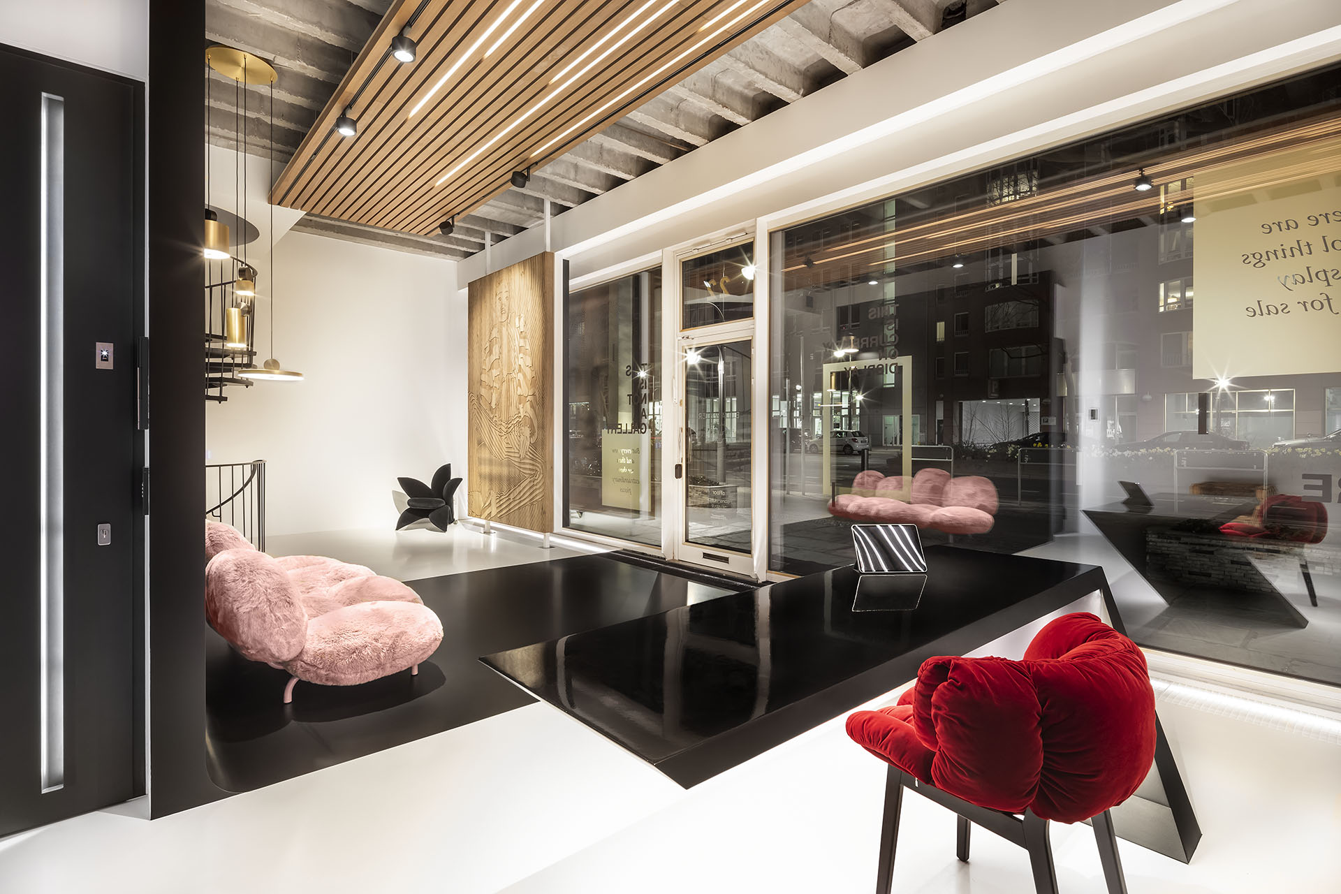 Innenansicht des Einrichtungshauses Budapester Salon mit einem knallroten Stuhl, rosa Plschsofa, schwarzen Elementen auf dem Biuden und Holzelementen an Wand und Decke