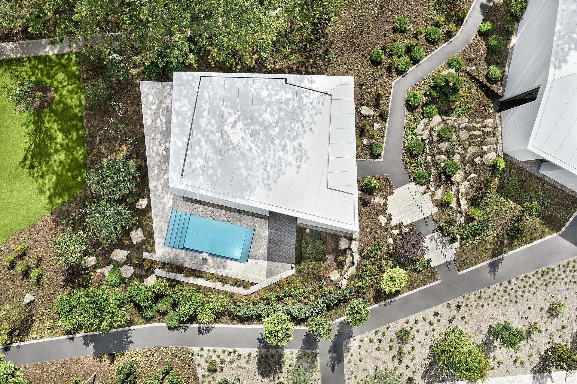 Luftaufnahme mit Blick senkrecht auf einen futuristischen weißen Bungalow in einer mordernen Gatrneanlage mit rechteckigigem Pool