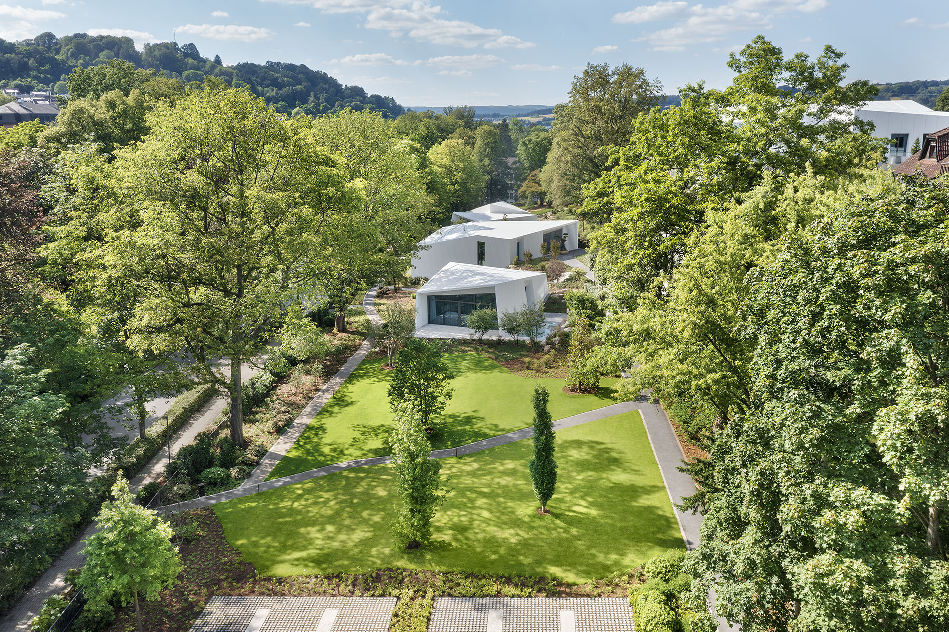 Futuristische weiße Bungalows in einem klar strukturierten Garten umgeben von hohen Bäumen