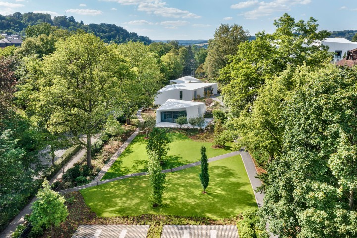 Futuristische weiße Bungalows in einem klar strukturierten Garten umgeben von hohen Bäumen