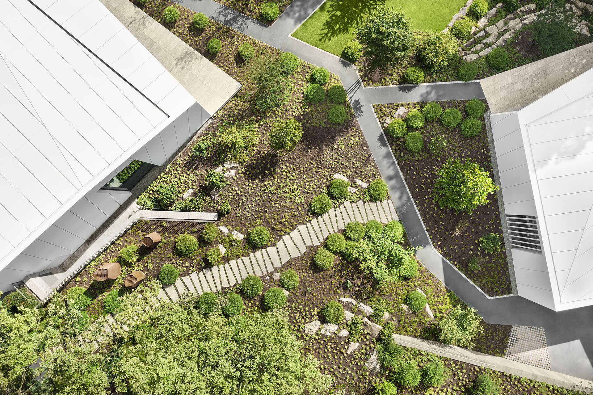 Luftaufnahme zweier futuristischer Bungalows, die durch eine klar strukturierte moderne Gartenlandschaft und einen Weg aus Sandsteinplatten miteinander verbunden sind