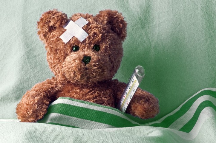 Brauner Teddy mit einem gekreuzten Pflaster auf der Stirn und einem Quecksilber-Fieberthermometer ungter dem Arm