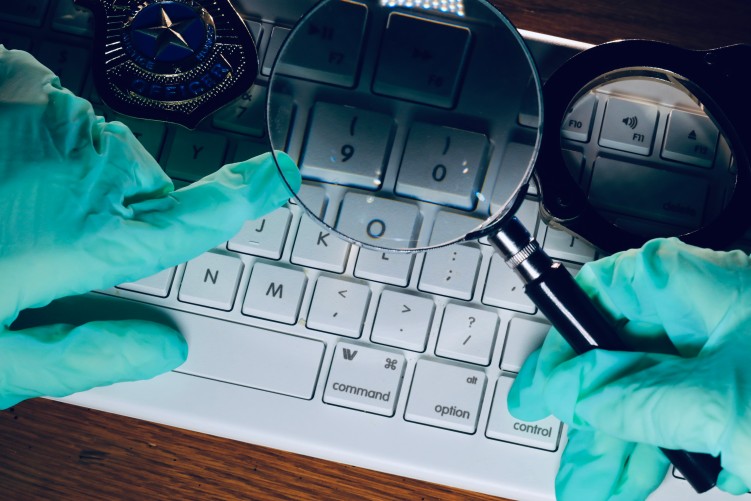 Hände mit grünen OP-Handschuhen halten eine Lupe über eine Tastatur