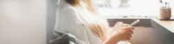 Frau, von der man nur die blonden Haare sieht,  hält ein Handy in der Hand und tippt etwas.