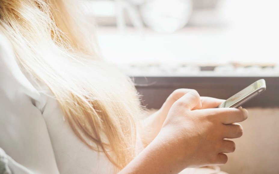 Frau, von der man nur die blonden Haare sieht,  hält ein Handy in der Hand und tippt etwas.
