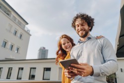 Mann und Frau schauen auf einer Dachterassse lachend auf sein Tablet