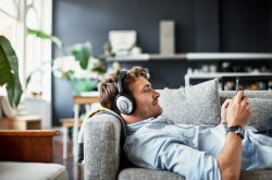 Ein junger Mann liegt auf einem Sofa und hört über Kopfhörer Musik.