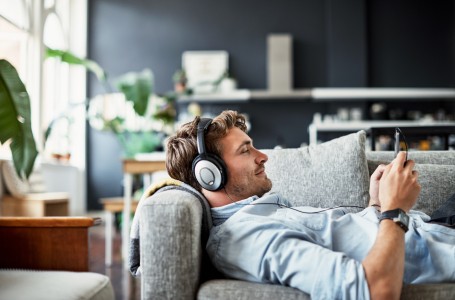 Ein junger Mann liegt auf einem Sofa und hört über Kopfhörer Musik.