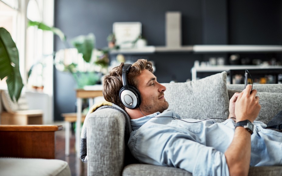 Ein junger Mann liegt auf einem Sofa und hört über Kopfhörer Musik.