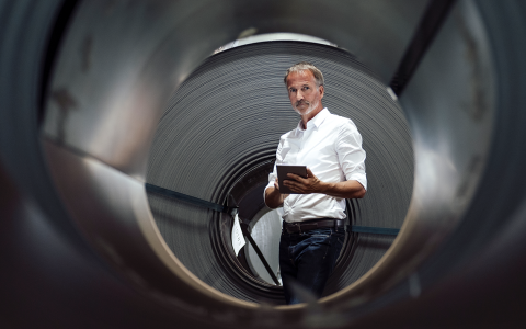 Mann mit weißem Hemd und grauem Bart steht mit einem Tablet in der Hand vor einer schwarzen Röhre