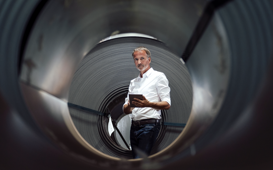 Mann mit weißem Hemd und grauem Bart steht mit einem Tablet in der Hand vor einer schwarzen Röhre