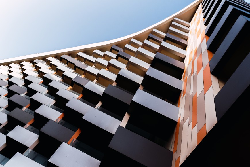 Moderne Architektur mit vielen schwarzen Balkonen und orange-weißen Paneelen als Außenfassade