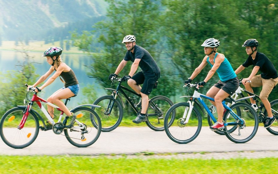 Vierköpfige Familie fährt auf Fahrrädern an einem Bergsee vorbei
